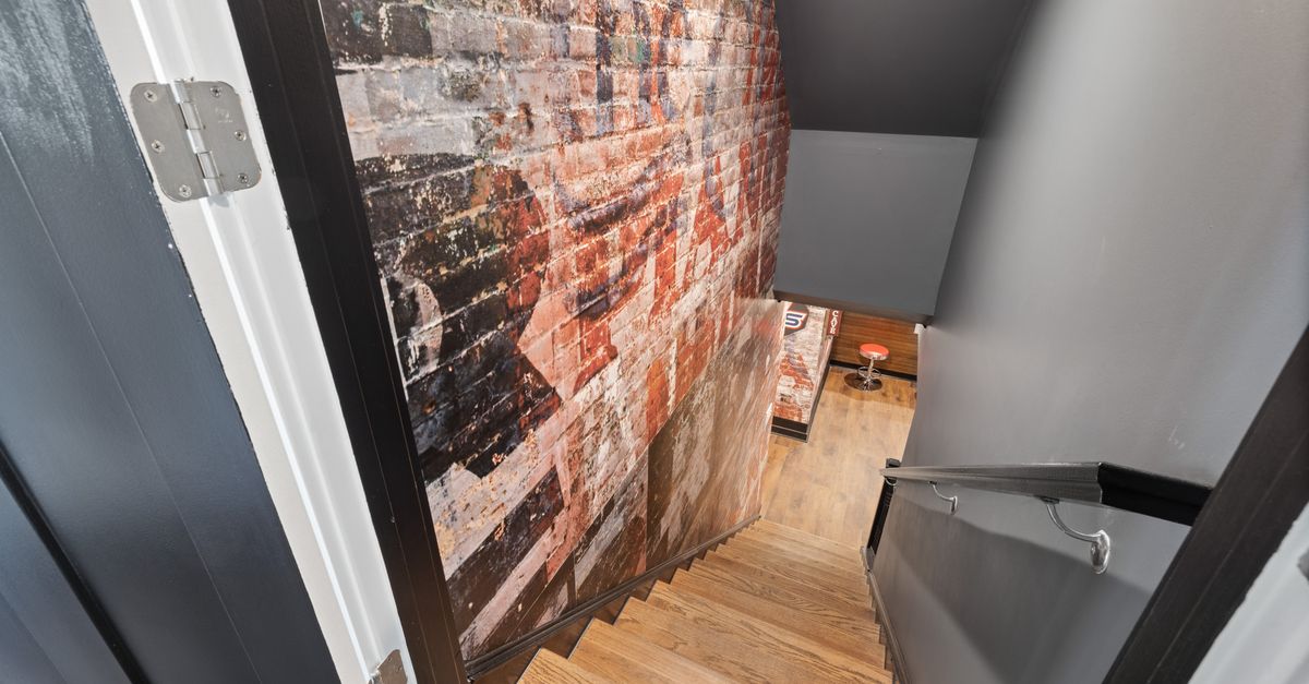 A modern staircase with exposed brick wall art leading to a stylish basement.